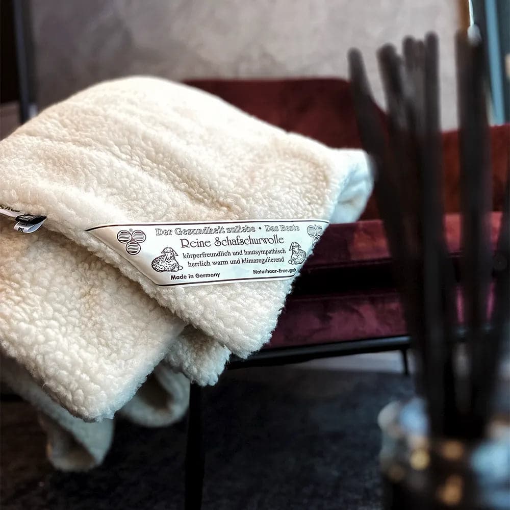 Ein Stapel mySheepi Bettdecken aus Schafschurwolle liegt auf einem Stuhl.