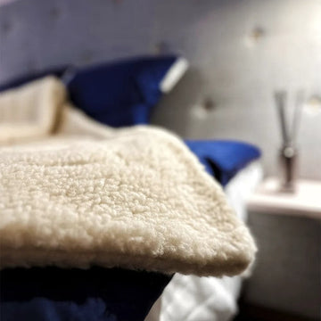Eine Nahaufnahme eines Bettes mit einer mySheepi Bettdecke aus Schafschurwolle darauf.