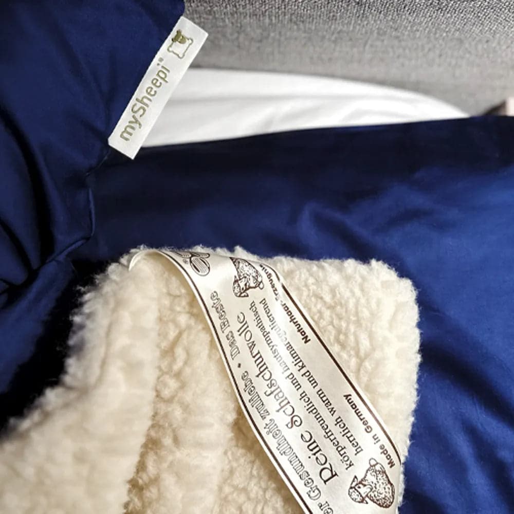 Eine mySheepi-Bettdecke aus Schafschurwolle mit dem mySheepi-Label darauf sitzt auf einem Bett.