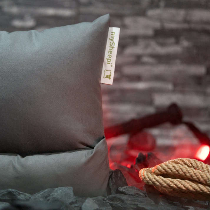 Eine Nahaufnahme eines mySheepi TRAVEL Nackenkissens in Berggrau inkl. REISETASCHE auf einem Bett.